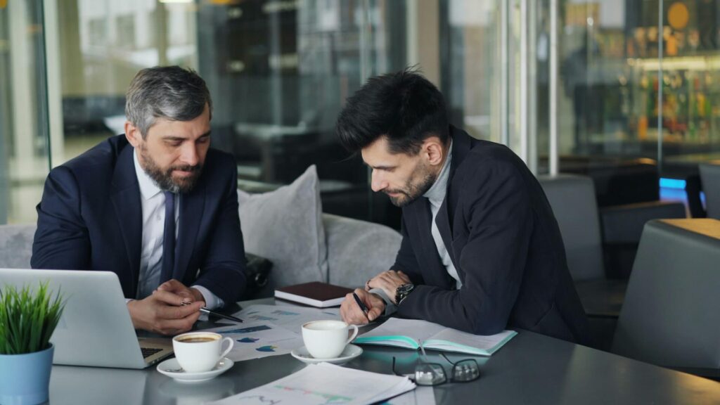 Dos profesionales analizando gráficos y datos en una mesa con café.